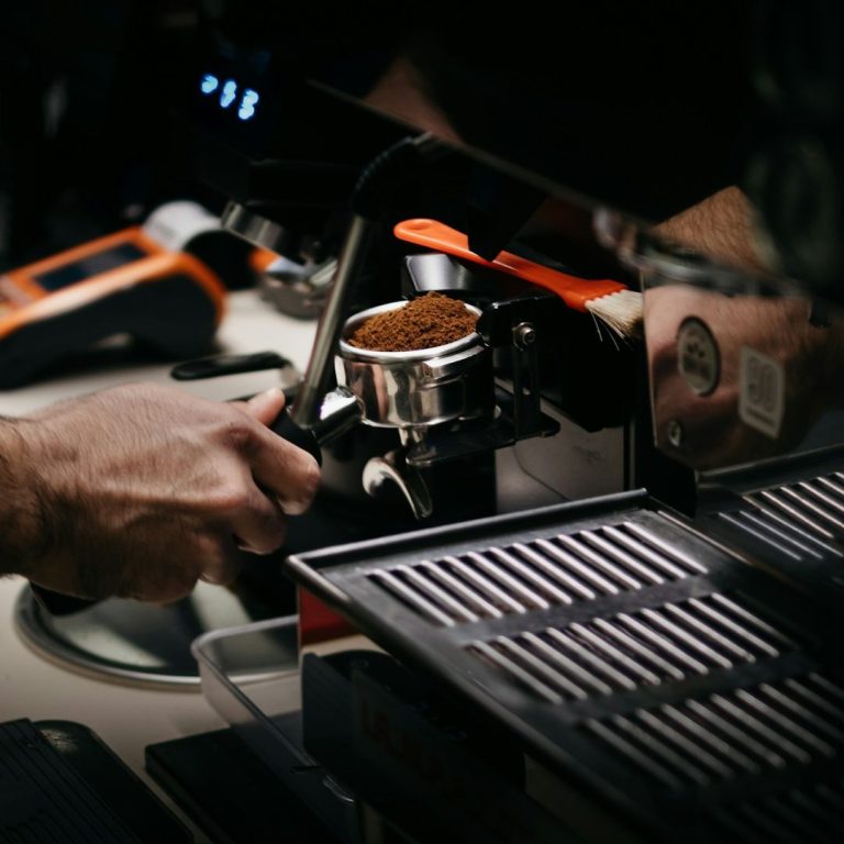 Eine Hand bereitet Espresso mit einer Siebträgermaschine in einer Kaffeebar.