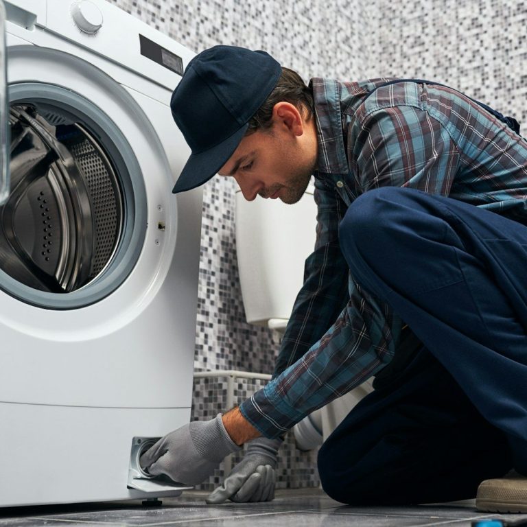 Mann repariert eine Waschmaschine in einem Badezimmer.