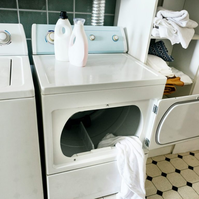 Weiße Waschmaschine mit geöffnetem Tür, daneben Waschmittelflaschen und Wäsche.