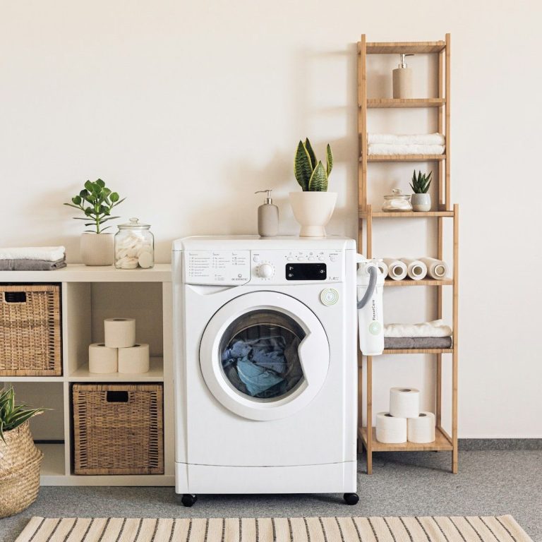 Weißes Waschmaschine steht neben einem Regal mit Pflanzen und Körben.