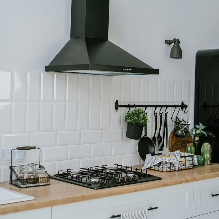 Moderne Küche mit Holzarbeitsplatte, Herd und schwarzer Dunstabzugshaube. Pflanze dekoriert.