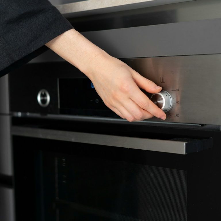 Eine Hand dreht einen Knopf an einem modernen Backofen.