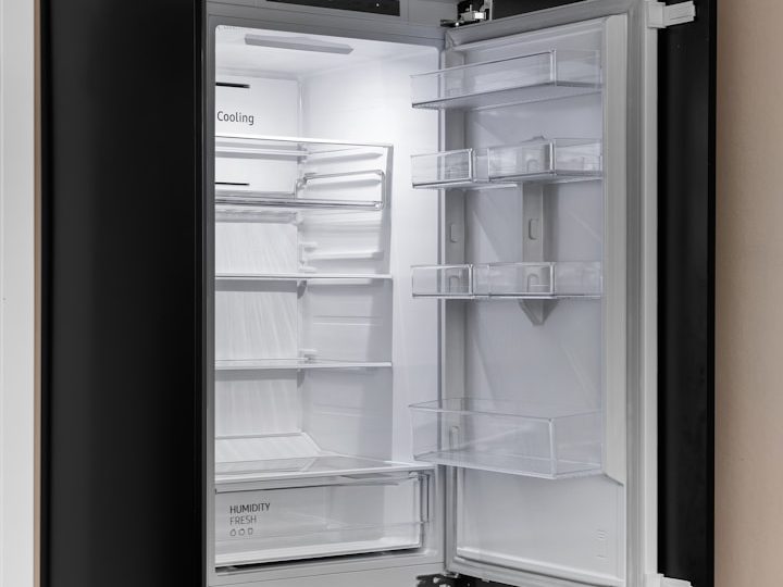 Ein geöffneter Kühlschrank mit leeren Regalen und einer hellen Beleuchtung.