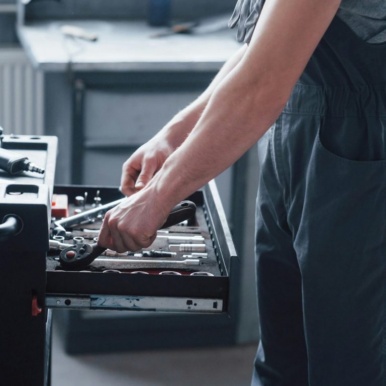 Person in Latzhose greift nach Werkzeug in einem geöffneten Werkzeugsatz.