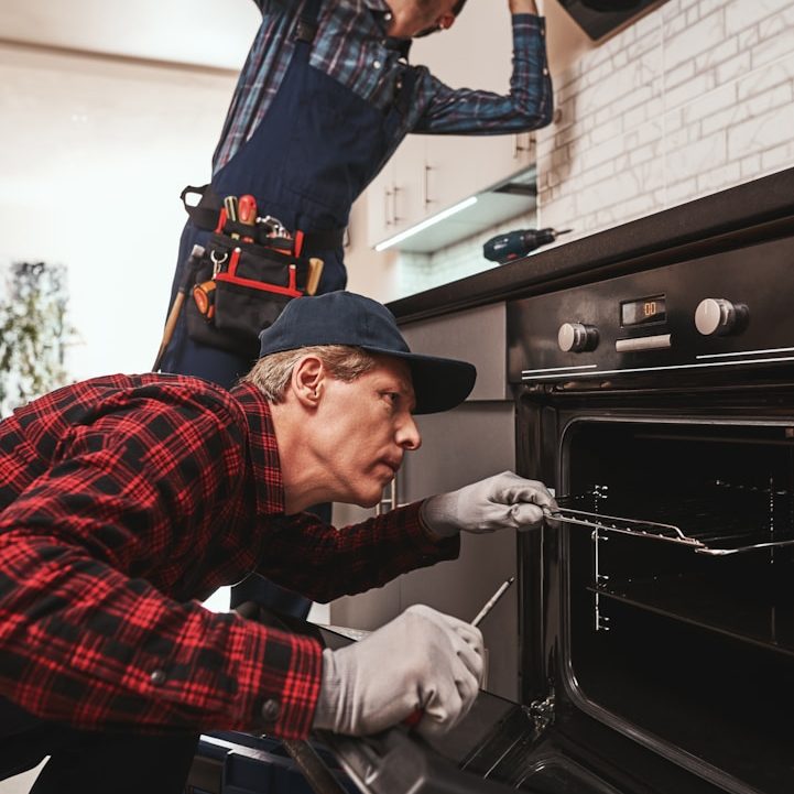 Zwei Handwerker reparieren gemeinsam einen Ofen in einer modernen Küche.