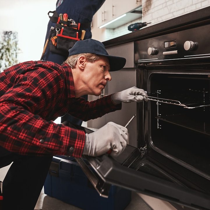 Ein Techniker überprüft einen Herd, trägt Handschuhe und ist konzentriert bei der Arbeit.